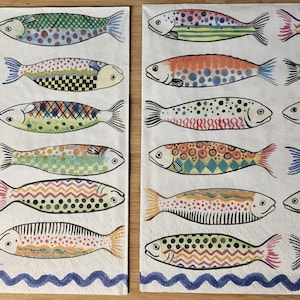 May include: Two rectangular decorative napkins with a repeating pattern of colorful fish. Each fish is uniquely designed with patterns and colors like orange, green, blue, and yellow. The napkins have a white background with a blue wavy border.