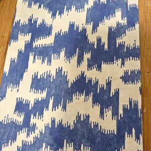 May include: A blue and white patterned fabric napkin with a blue border. The pattern is a repeating design of abstract shapes.