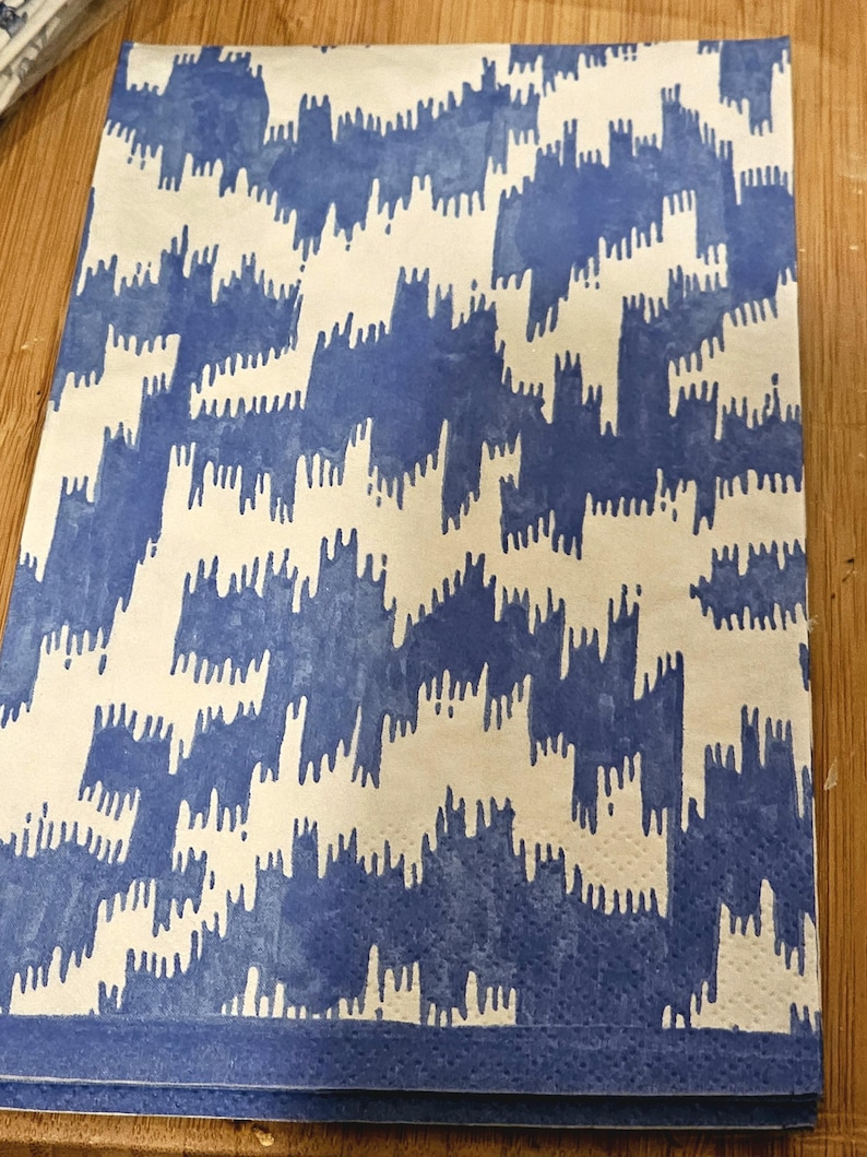 以下が含まれることがあります： 青と白の模様の布製のナプキンで、青い縁取りがあります。模様は抽象的な形を繰り返したデザインです。