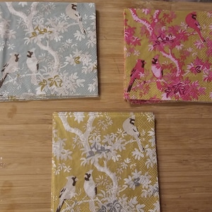 May include: Three decorative paper napkins with a floral pattern and birds. The napkins are in shades of blue, yellow, and pink.