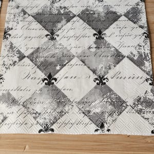 May include: Black and white patterned paper napkin with a fleur-de-lis design and a handwritten inscription that reads "Raif/jan-N. Paris".