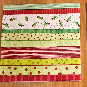 May include: A square paper napkin featuring horizontal bands of various patterns including green holly leaves with red berries, red and green stripes, and polka dots in red and green colors on a white and light green background.