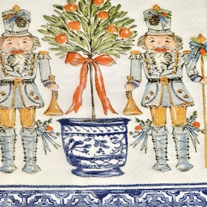 May include: Two blue and white nutcracker figurines stand on either side of a potted orange tree with red ribbon. The tree is in a blue and white patterned pot. The background is white with a blue and white patterned border.