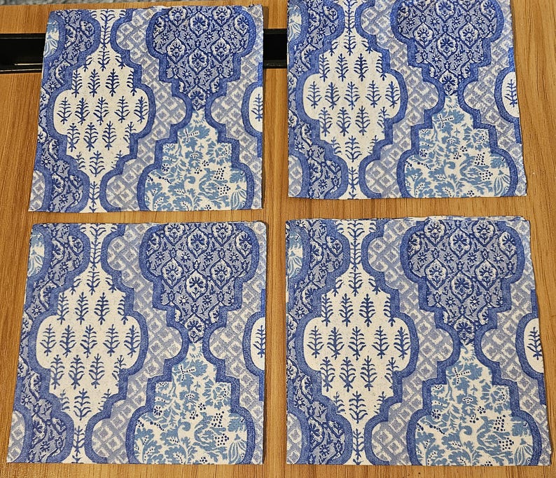Op de afbeelding: Vier vierkante onderzetters met een herhalend blauw-wit patroon. Het ontwerp bestaat uit complexe, in elkaar grijpende geometrische vormen gevuld met gestileerde bloemen- en plantmotieven, wat zorgt voor een samenhangend visueel thema voor alle vier.