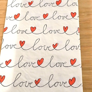 May include: White paper napkins with a repeating pattern of red hearts and the word "love" written in black cursive.