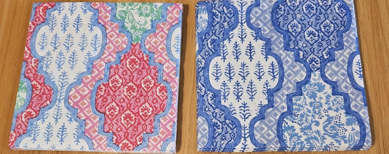 Op de afbeelding: Twee vierkante servetten met een herhalend ogee-patroon. Het linker servet toont roze, lichtblauwe en groene bloemmotieven. Het rechter servet heeft een monochroom blauw-wit ontwerp met gedetailleerde botanische en geometrische patronen.
