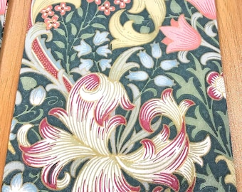 May include: Rectangular decorative fabric with a floral pattern. The design features large, stylized flowers in shades of pink and cream, set against a dark teal background. The edges are trimmed with a light blue border. The overall aesthetic is reminiscent of vintage textiles.