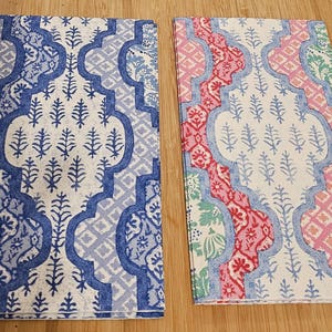 May include: Two fabric placemats with a white background and a blue and white geometric pattern on the left and a pink, green, and white geometric pattern on the right.
