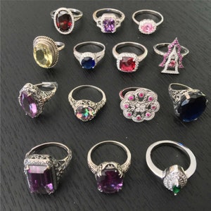 May include: A collection of 15 silver rings with various colored gemstones, including purple, red, blue, yellow, and green. The rings are set with intricate filigree designs and feature a variety of gemstone shapes.