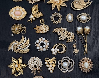 May include: A collection of 20 vintage brooches featuring a variety of designs, including floral, geometric, and animal motifs. The brooches are made of gold-tone metal and adorned with faux pearls.