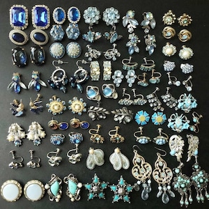 Könnte beinhalten: Eine große Sammlung von blauen und silbernen Ohrringen. Die Ohrringe sind aus verschiedenen Materialien gefertigt, darunter Metall, Glas und Kunststoff. Einige der Ohrringe sind mit Strasssteinen, Perlen und anderen Verzierungen verziert.