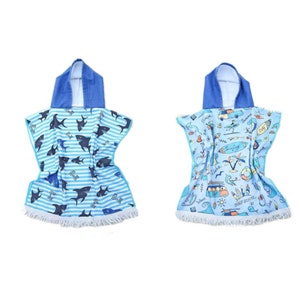 May include: Two hooded towels with fringe trim. One towel features a blue and white striped pattern with sharks. The other towel features a blue and white pattern with a beach scene and the text "Surfing".