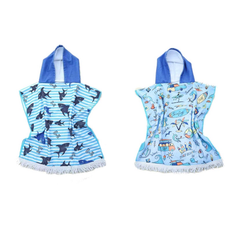 May include: Two hooded towels with fringe trim. One towel features a blue and white striped pattern with sharks. The other towel features a blue and white pattern with a beach scene and the text "Surfing".