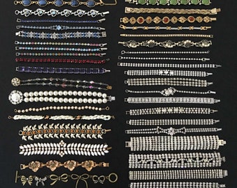 May include: A collection of 20 vintage bracelets featuring a variety of styles and colours, including pearl, crystal, and rhinestone. The bracelets are displayed in rows against a black backdrop.