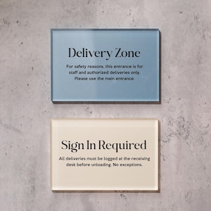 May include: Two rectangular signs on a gray wall. The top sign is light blue and reads "Delivery Zone." The bottom sign is off-white and reads "Sign In Required."