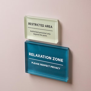 May include: Two rectangular signs are mounted on a pink wall. The top sign reads "RESTRICTED AREA" with the text "Authorized personnel only beyond this point." The bottom sign says "RELAXATION ZONE" and "PLEASE RESPECT PRIVACY."