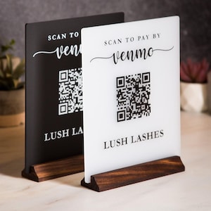 May include: Two acrylic signs with wooden bases. One is black, the other white. Both read "Scan to pay by Venmo" and "Lush Lashes" with a QR code. The signs are on a light-colored surface.