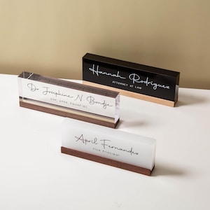Peut inclure: Trois plaques de bureau rectangulaires avec des bases en bois. Une est en acrylique transparent avec Dr. Josephine N. Bondje, DNP, APRN, PMHNP-BC. Une est en acrylique noir avec Hannah Rodriguez, Attorney at Law. Une est en acrylique dépoli avec April Fernandez, Vice Principal.