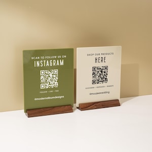 May include: Two informational signs with QR codes. One is olive green with "Scan to follow us on Instagram" and the other is off-white with "Shop our products here". Both are on wooden bases.