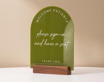 May include: A green arched sign with the words "WELCOME PATIENTS" at the top and "please sign-in and have a seat" in the centre. The sign is mounted on a rectangular wooden base. The words "THANK YOU!" are at the bottom.