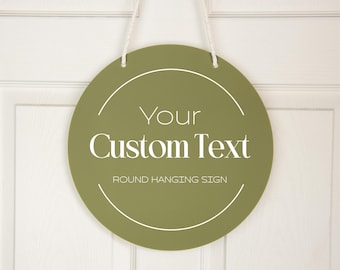 May include: A round, olive green hanging sign with a white rope for hanging. The sign has a white circle with the text "Your Custom Text" and "ROUND HANGING SIGN" in white.