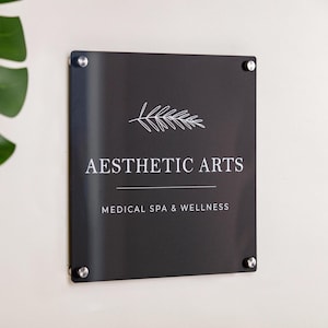 May include: Black sign with white text and a stylized branch design. The sign reads "Aesthetic Arts Medical Spa & Wellness".