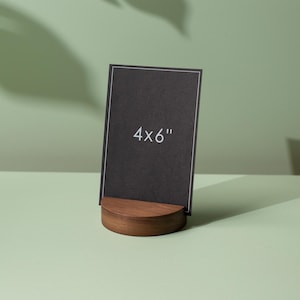 May include: A black 4x6" (10x15 cm) photo or card holder. The black card has a white border and the text "4x6" in white. The holder is made of a dark wood with a curved, half-moon shape.