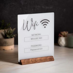 May include: White acrylic sign with black text and a wifi symbol. The sign reads "Wifi", "Network: MUUJEE Wifi", and "Password: Password 123!" The sign is on a wooden stand.
