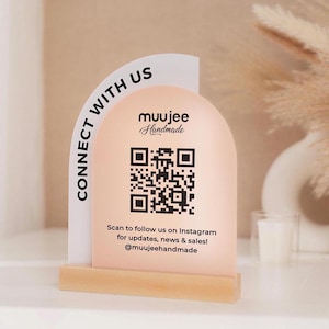 May include: A peach-colored arch-shaped sign with the text "CONNECT WITH US" and a QR code. The sign also includes the text "muujee Handmade" and instructions to follow on Instagram for updates and sales. It is mounted on a wooden base.