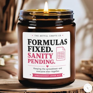 May include: A brown glass jar candle with a lit wick and a white label featuring the text: THE ARTFUL CRAFTS CO, FORMULAS FIXED. SANITY PENDING., a spreadsheet icon, and the text: Keeping the spreadsheet—and everyone else—together. SPREADSHEET LOVER GIFT.