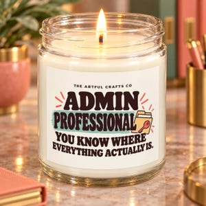 Puede incluir: Una vela en frasco de vidrio transparente con cera blanca y una mecha encendida. La etiqueta muestra el texto THE ARTFUL CRAFTS CO, ADMIN PROFESSIONAL y YOU KNOW WHERE EVERYTHING ACTUALLY IS, con un gráfico de una carpeta y una llave roja.