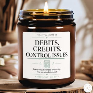 Op de afbeelding: Een bruine glazen potkaars met een brandende lont en een wit etiket met de tekst: THE ARTFUL CRAFTS CO, DEBITS. CREDITS. CONTROL ISSUES., een rekenmachine-icoon en de tekst: Everything balances eventually. The workload does not.