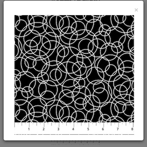 May include: Black fabric with a repeating pattern of white overlapping circles. The circles vary in size and create a dynamic, abstract design. The fabric has a ruler along the bottom edge.
