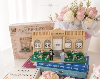 Puede incluir: Una exhibición con un modelo Lego de Pemberley, libros de Jane Austen, cupcakes y un ramo de rosas. La escena incluye el texto "PEMBERLEY, but make it yours" y "books, tea & quiet dreams."