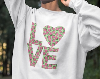 May include: White sweatshirt with a strawberry-themed "LOVE" graphic. The letters are filled with a pink strawberry pattern on a green background, and the "O" is a heart shape with the same strawberry design. The sweatshirt is a casual, comfortable style.