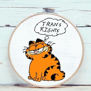 May include: Cross-stitch pattern featuring a cartoon orange cat with black stripes, thinking a thought bubble that says "TRANS RIGHTS".