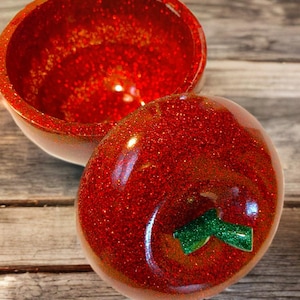 Könnte beinhalten: Eine rote, glitzernde Apfel-Schmuckschatulle mit einem grünen, glitzernden Stiel. Die Schachtel ist geöffnet und das Innere ist ebenfalls rot glitzernd.