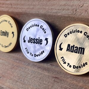 May include: Three gold, silver, and brass decision coins with the words "Decision Coin" and the names "Emily", "Jessie", and "Adam" on them. Each coin has an arrow pointing to the left and right.