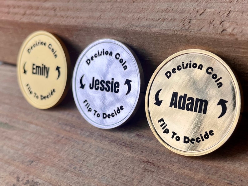 May include: Three gold, silver, and brass decision coins with the words "Decision Coin" and the names "Emily", "Jessie", and "Adam" on them. Each coin has an arrow pointing to the left and right.