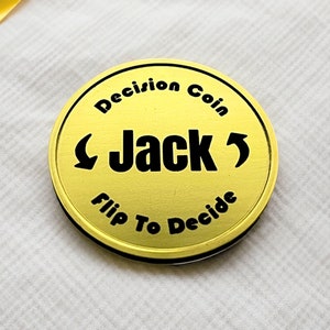 May include: A gold-colored coin with the text "Decision Coin" and "Flip To Decide" around the edge. The word "Jack" is in the center with arrows pointing left and right.