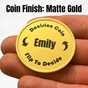 May include: A gold-colored coin with the text "Decision Coin" and "Flip To Decide" around the edge. The name "Emily" is in the center of the coin.