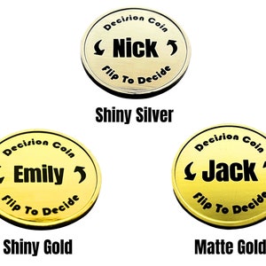 May include: Three gold-colored decision coins with the words "Decision Coin" and "Flip To Decide" around the edge. The coins feature the names "Nick", "Emily", and "Jack" in black lettering. The coins are labeled "Shiny Silver", "Shiny Gold", and "Matte Gold".