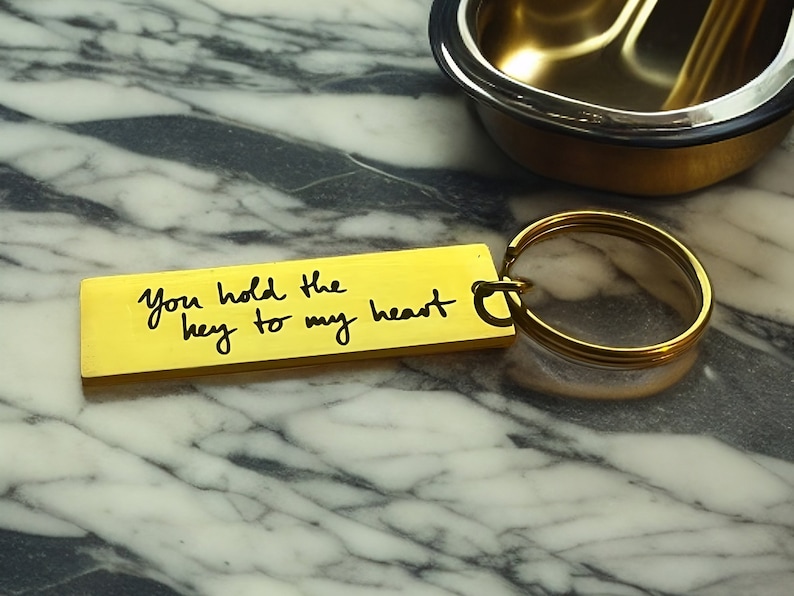 Op de afbeelding: Een gouden sleutelhanger met een rechthoekig label waarop staat "You hold the key to my heart".