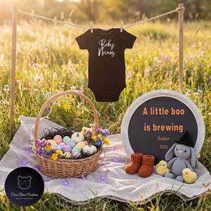 May include: A black baby onesie with the text "Baby Nunez" hangs on a clothesline. A wicker basket filled with pastel-colored eggs, flowers, and pumpkins sits on a blanket. A chalkboard sign reads "A little boo is brewing" with baby booties and a stuffed bunny.