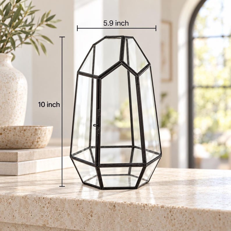 Puede incluir: Un terrario de vidrio geom&eacute;trico con marco de metal negro, que presenta una puerta con bisagras y una forma pentagonal irregular facetada. La estructura mide 25,4 cm de alto y 15 cm de ancho, ofreciendo una vista clara a trav&eacute;s de sus paneles.