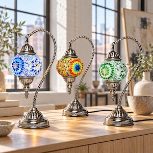 May include: Three table lamps with curved, twisted metal stands and antique silver-tone bases. Each lamp features a globe-shaped shade crafted from colorful mosaic glass tiles in blue, multi-colored, and green patterns with metal accents.