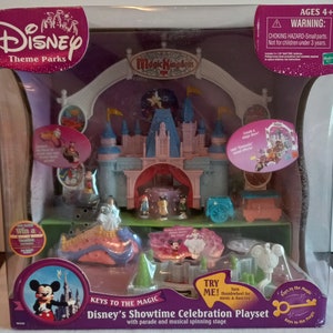 Puede incluir: Un set de juego Disney's Showtime Celebration con un castillo rosa y azul de Magic Kingdom con un escenario giratorio, un desfile y una llave mágica. El set de juego incluye a Mickey Mouse, Cenicienta y otros personajes de Disney.