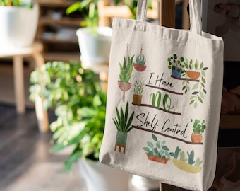 May include: Cream canvas tote bag with a plant illustration and the text "I Have No Shelf Control". The bag is hanging on a wooden rack with magazines. The background shows more plants.