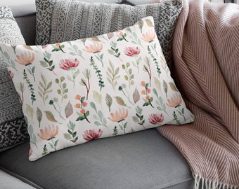 May include: A gray couch with a pink and white throw blanket and a floral patterned pillow. The pillow has a white background with pink and green flowers and leaves.