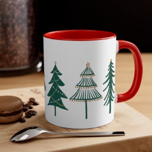 May include: White ceramic mug with a red rim and handle. The mug features a design of four stylized Christmas trees with gold accents.